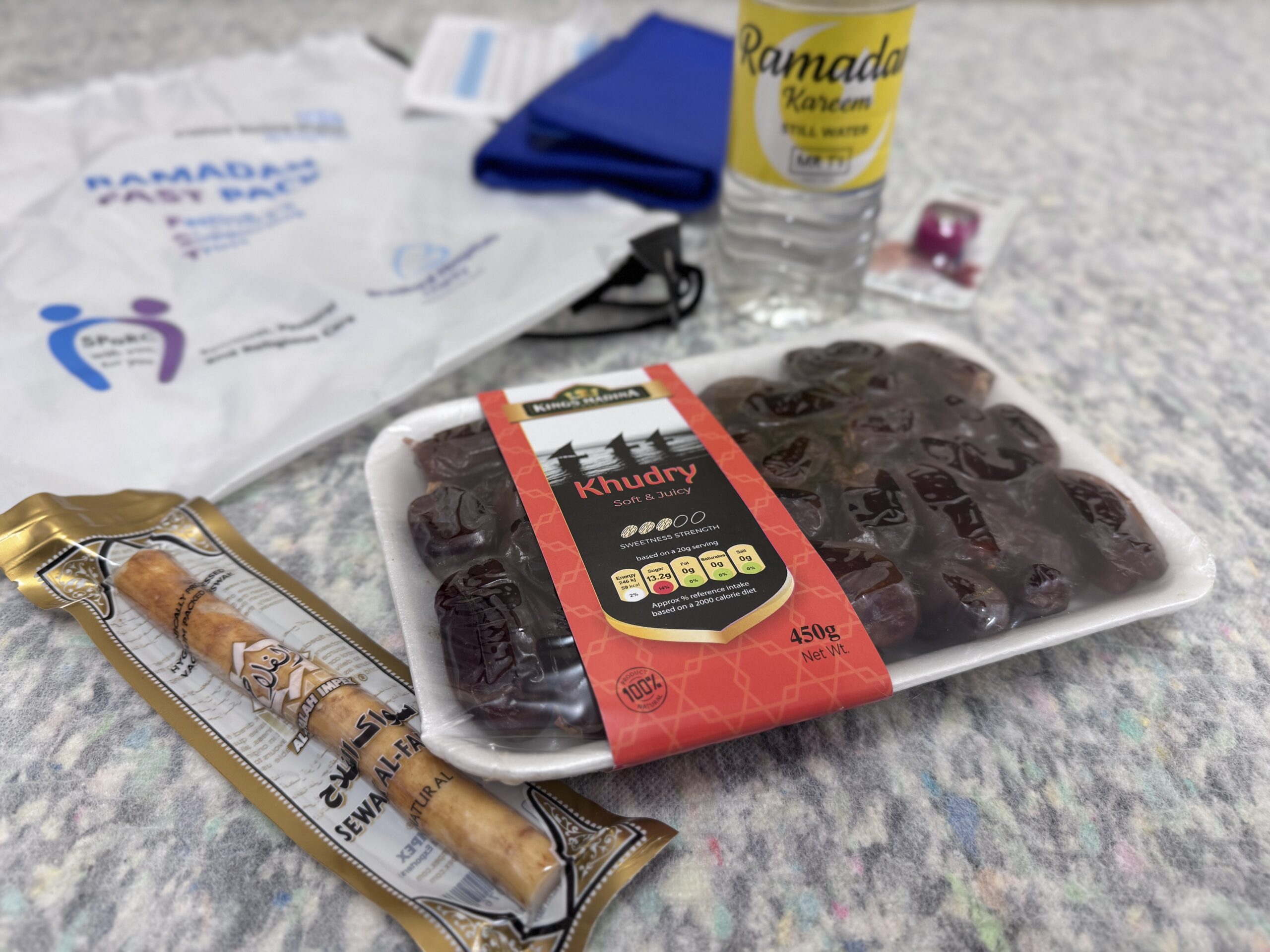 A FAST pack bag with the contents on display, including dates, a bottle of water, a snack, prayer times, prayer counter and thermal pack.